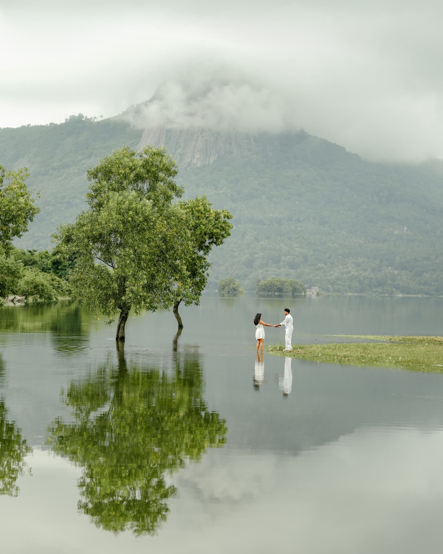 A couple standing in the shallows of a peaceful mountain lake